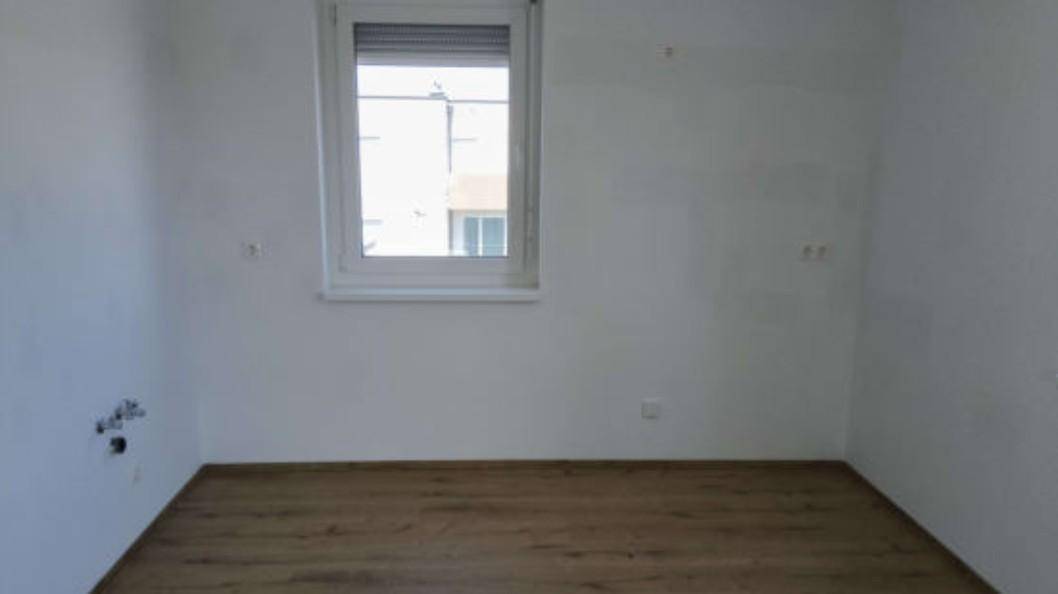 Leerer Raum mit Laminatboden und Fenster, vorbereitet für eine Kücheninstallation.