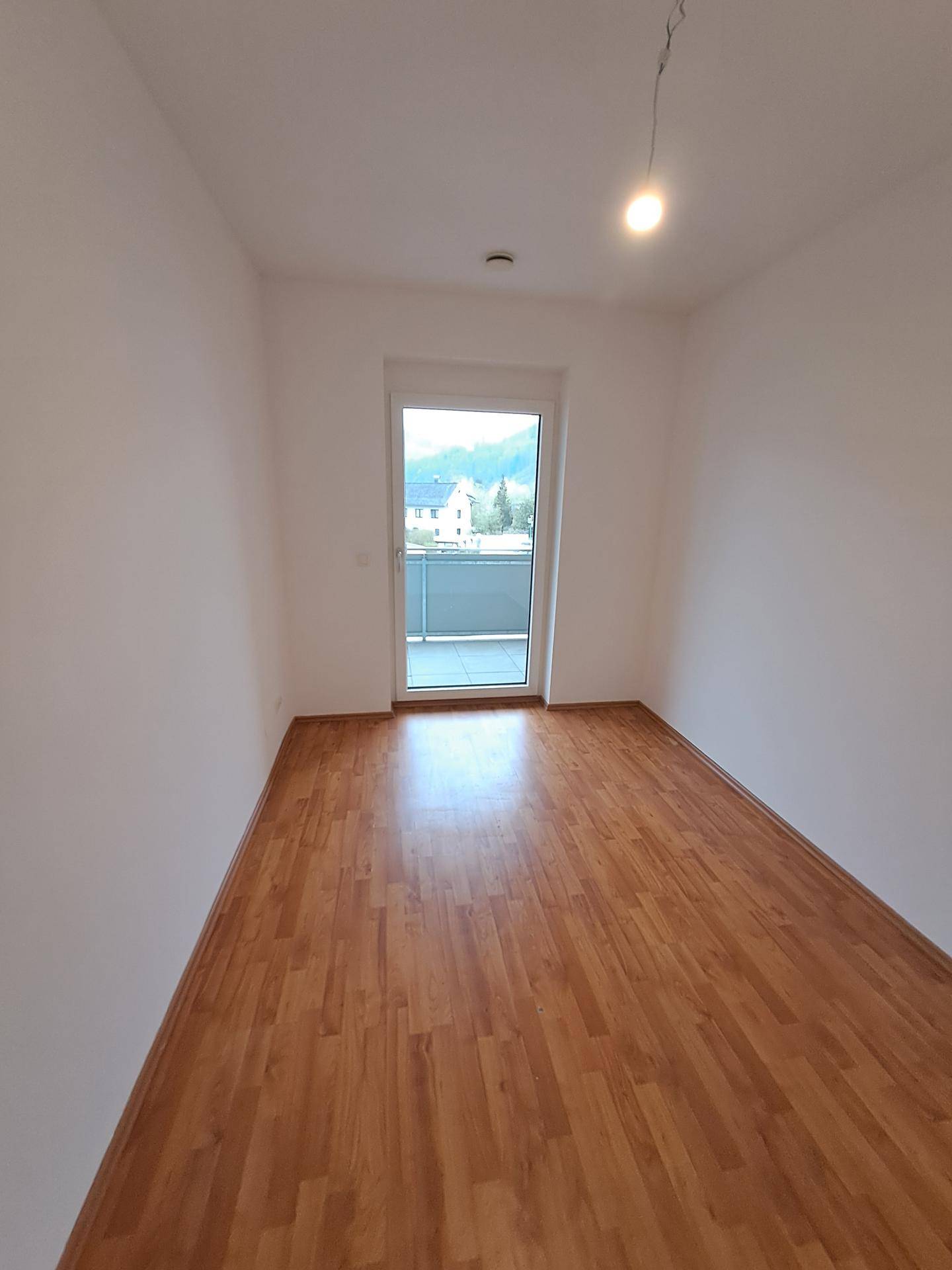 Helles Zimmer mit Laminatboden und Zugang zu einem Balkon, ideal als Schlafzimmer.