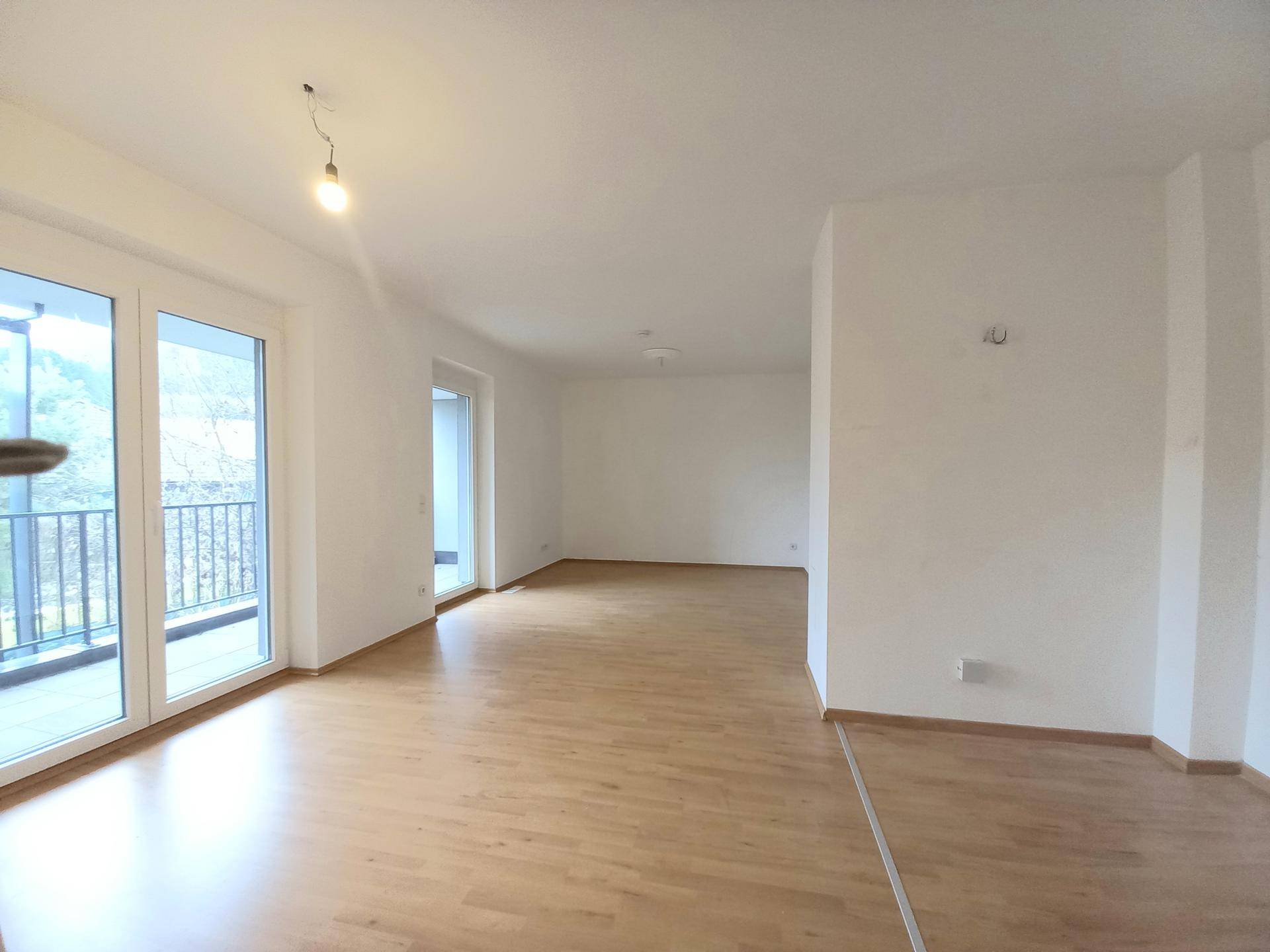 Heller, leerer Wohnraum mit Laminatboden und Zugang zu einem Balkon.