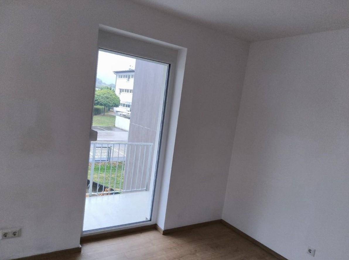 Helles Zimmer mit Laminatboden und bodentiefem Fenster mit Balkonzugang.