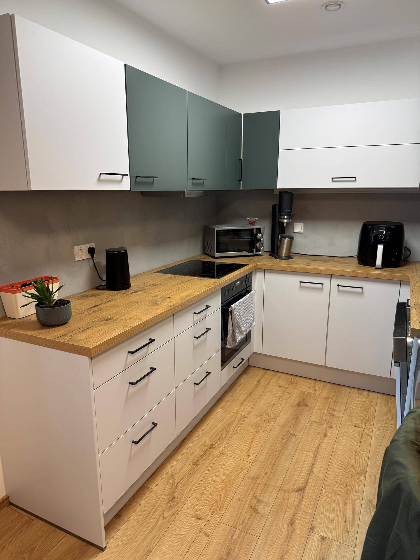 Moderne Küche mit weißen und graugrünen Schränken, Holzarbeitsplatte und Laminatboden.