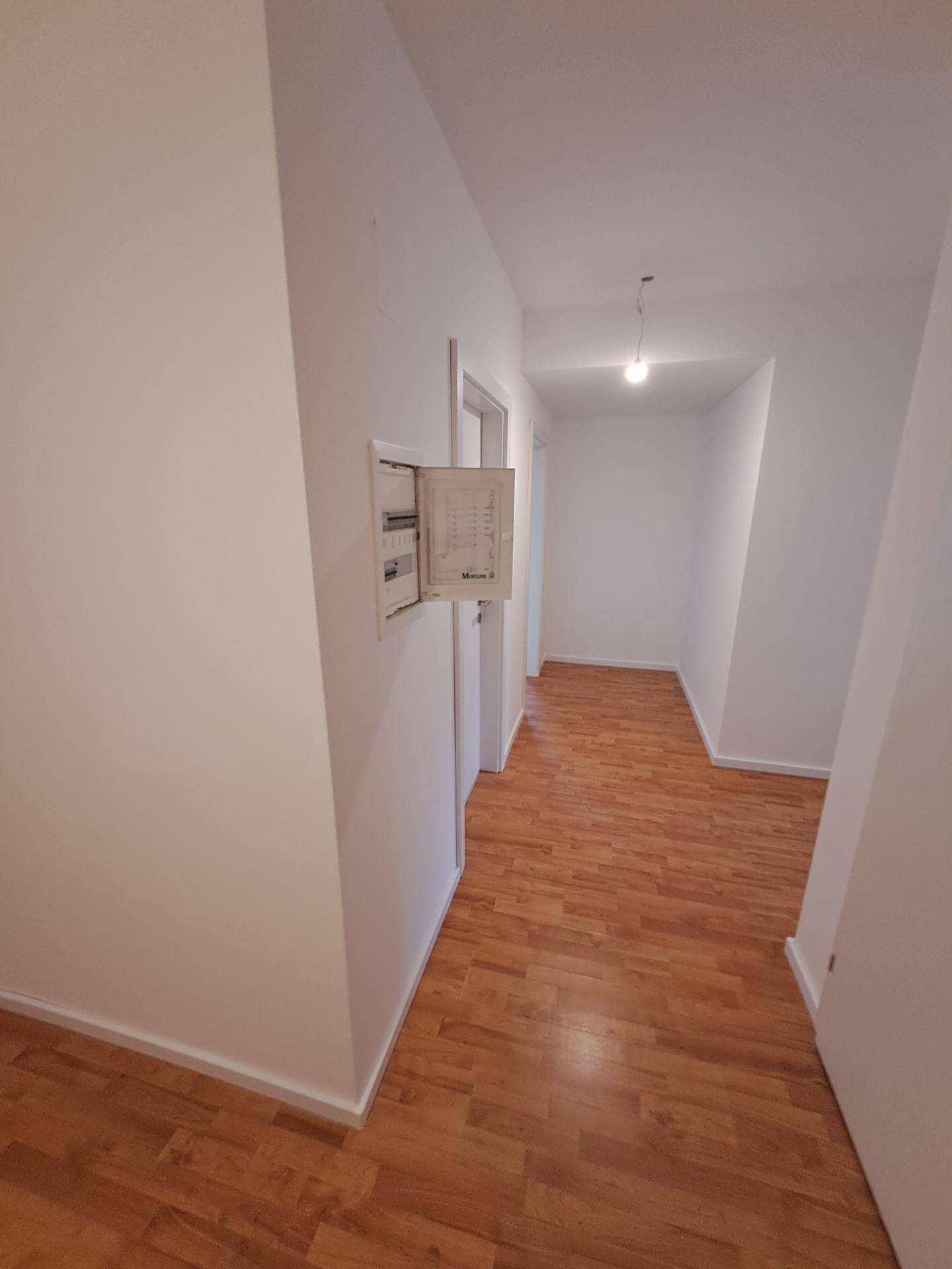 Heller Flur mit Laminatboden und weiß gestrichenen Wänden in einem modernen Gebäude.