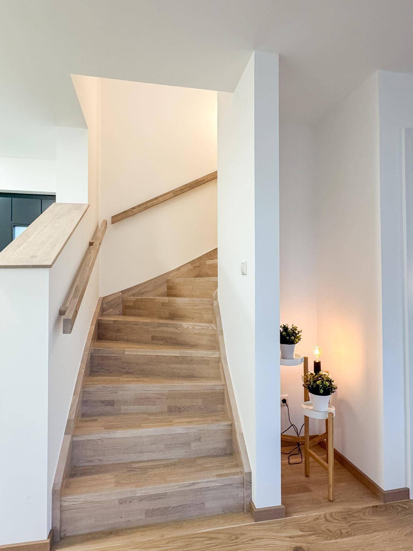 Helles Treppenhaus mit Holzstufen und passendem Handlauf, das die Etagen verbindet.