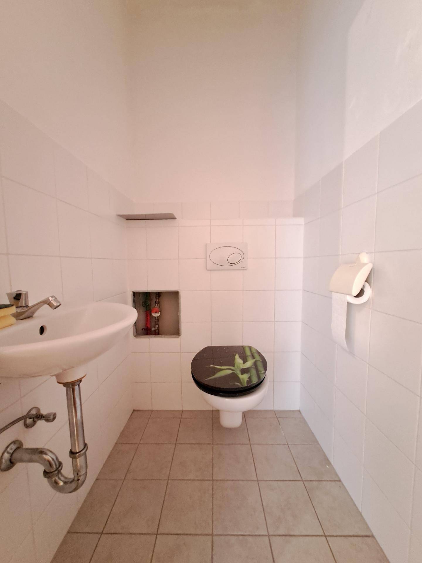 Kleines, gefliestes WC mit Waschbecken und Toilette.
