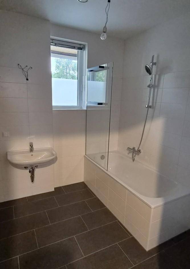 Modernes Badezimmer mit Badewanne, Dusche, Waschbecken und Fenster für Tageslicht.