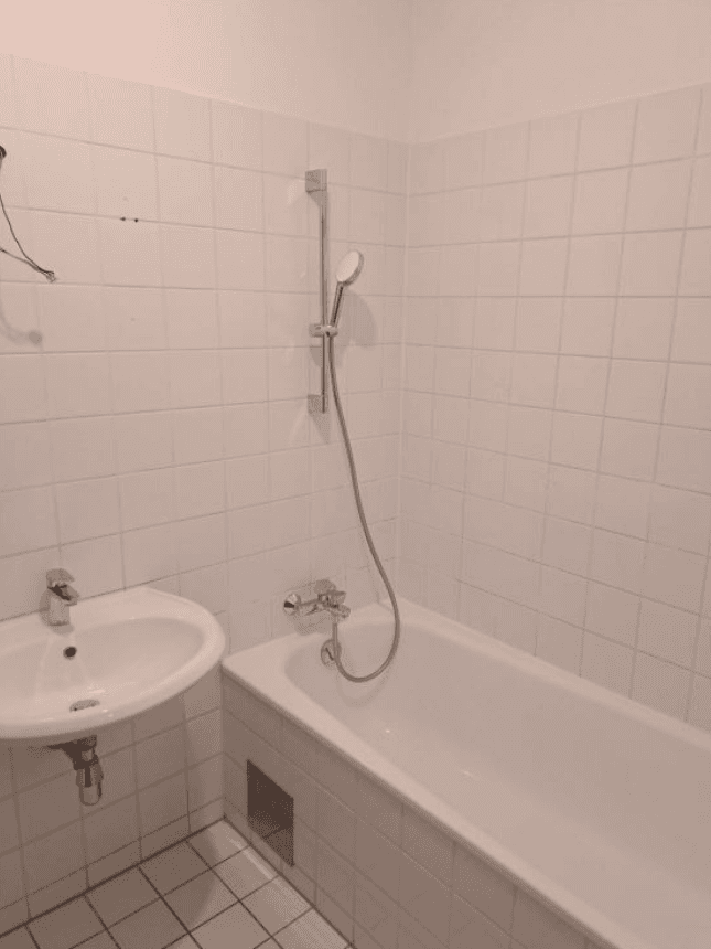 Helles Badezimmer mit weißen Fliesen, Badewanne mit Duschfunktion und einem einzelnen Waschbecken.
