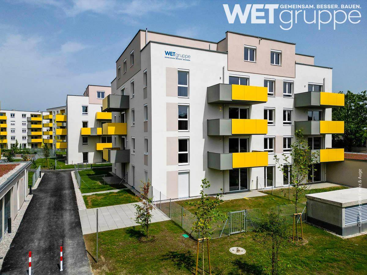 Neubau-Wohngebäude mit markanten gelben Balkonen und gepflegter Außenanlage.