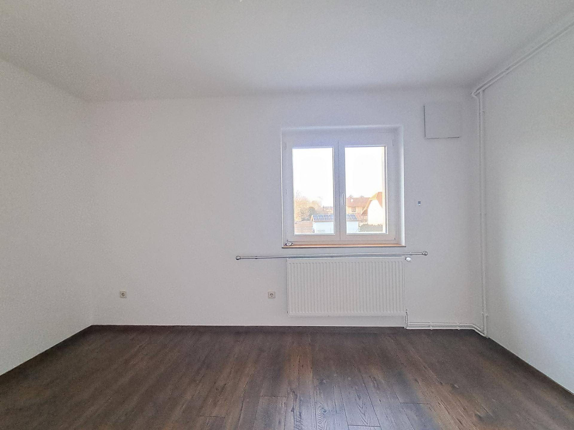 Helles Zimmer mit Laminatboden und einem großen Fenster, bereit zur individuellen Gestaltung.