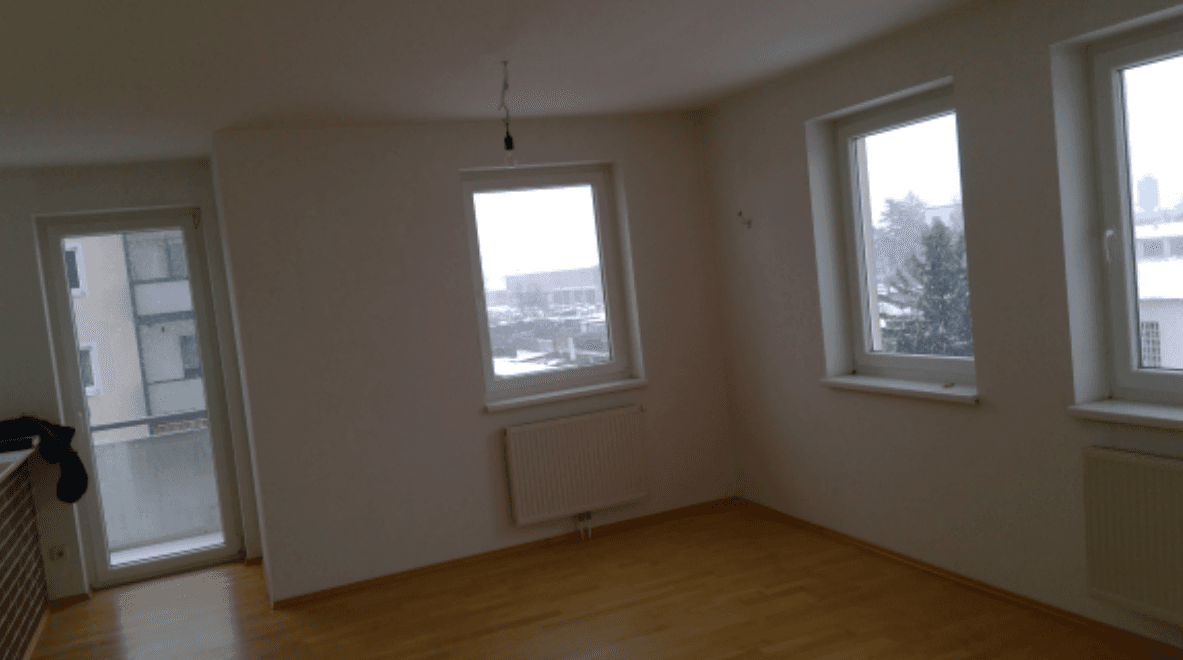 Heller, leerer Wohnraum mit Holzboden, großen Fenstern und Balkonzugang, ideal für natürliches Licht.