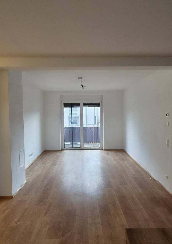 Heller Wohnbereich mit Laminatboden und Zugang zu einem Balkon oder einer Terrasse.