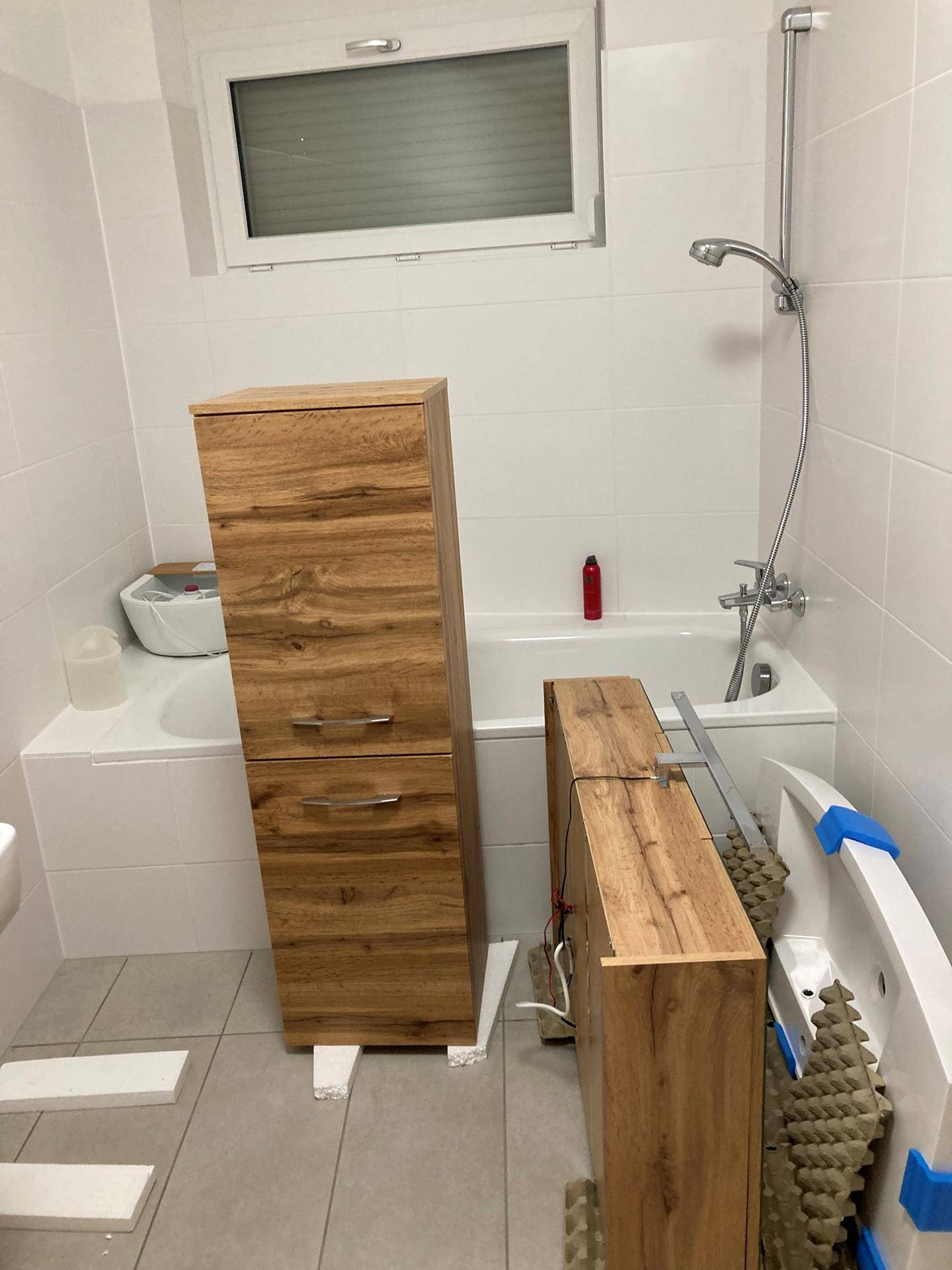 Modernes Badezimmer mit Badewanne, Fenster und Holzschränken, teilweise noch im Aufbau.