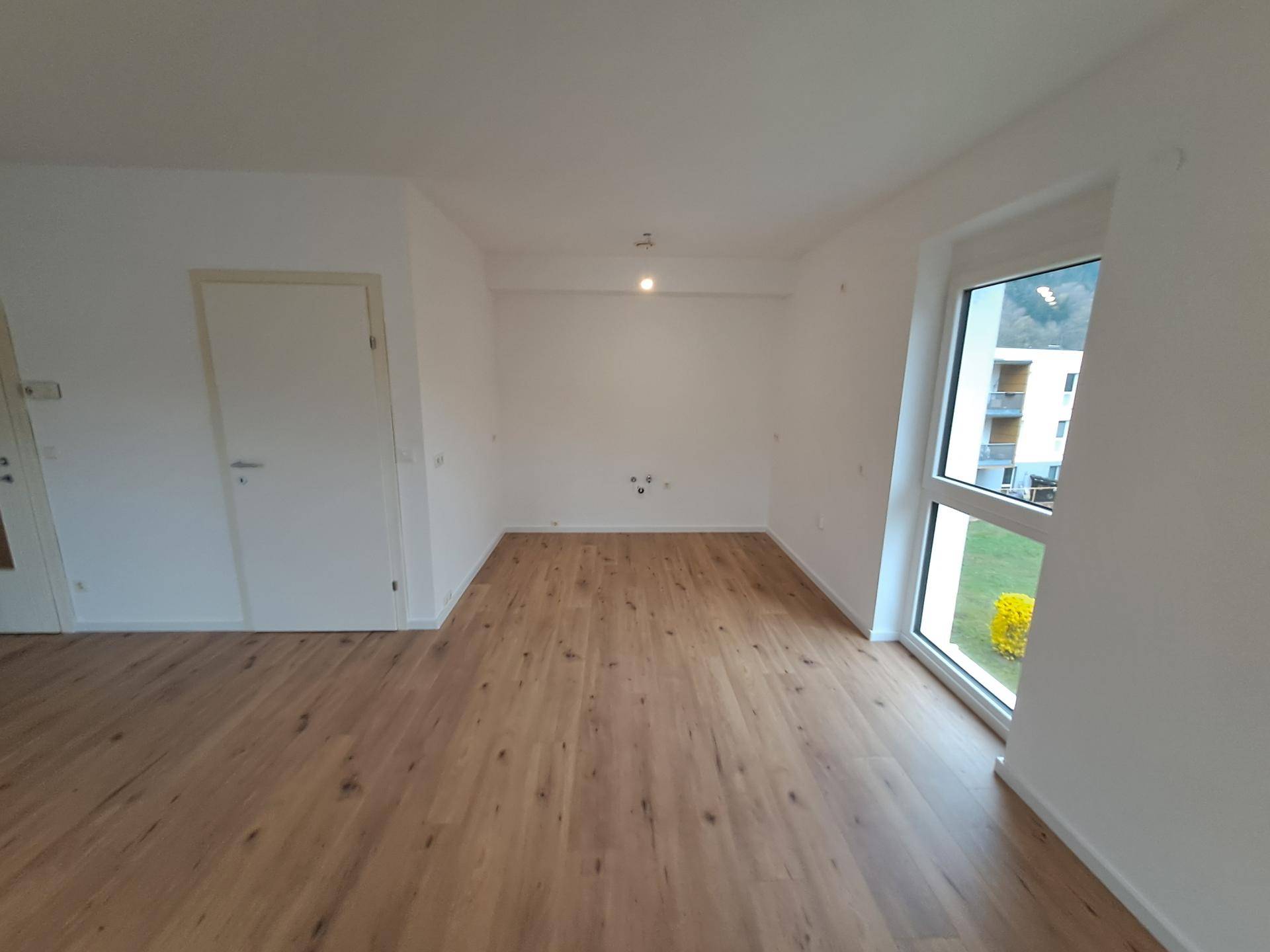 Heller Wohnbereich mit Holzboden und großem Fenster, das viel natürliches Licht hereinlässt.