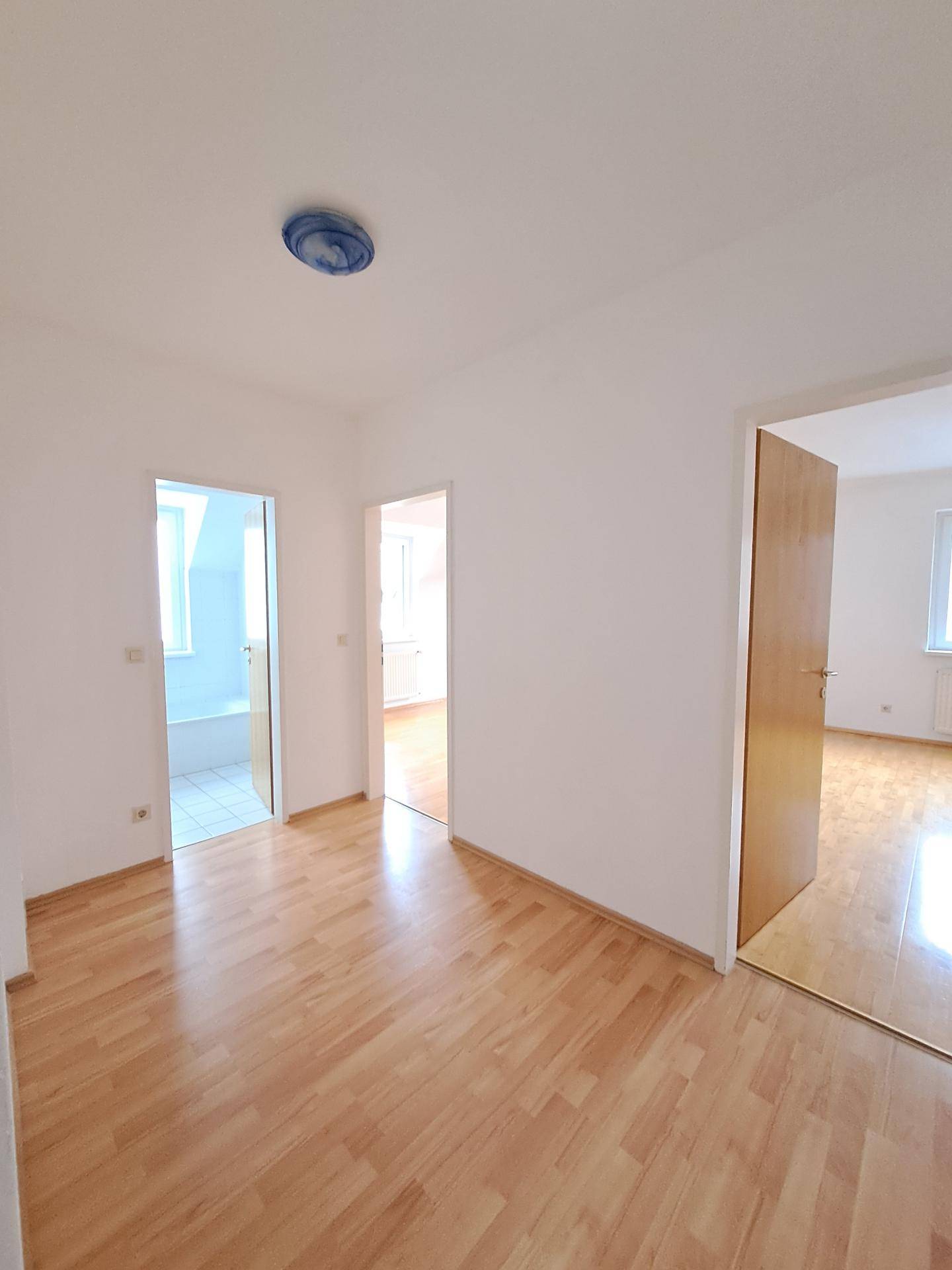 Heller Flur mit Laminatboden und Zugängen zu verschiedenen Zimmern, inklusive Badezimmer und weiteren Räumen.