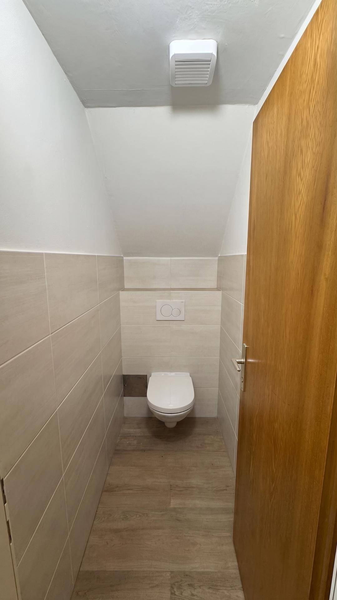 Modernes Gäste-WC mit Wand-WC, beigefarbenen Fliesen und Laminatboden.