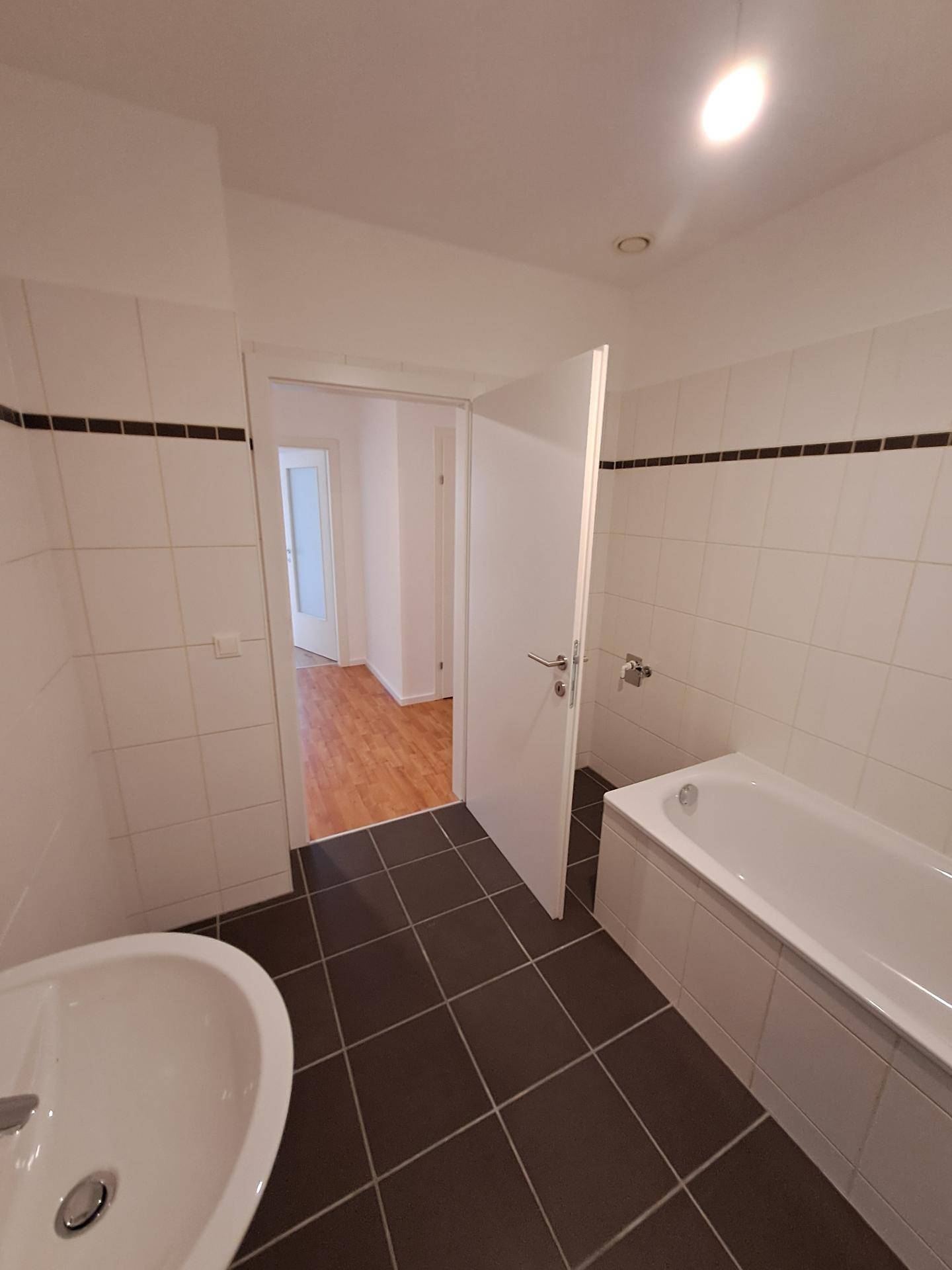 Modernes Badezimmer mit Badewanne, Waschbecken und dunklen Bodenfliesen.