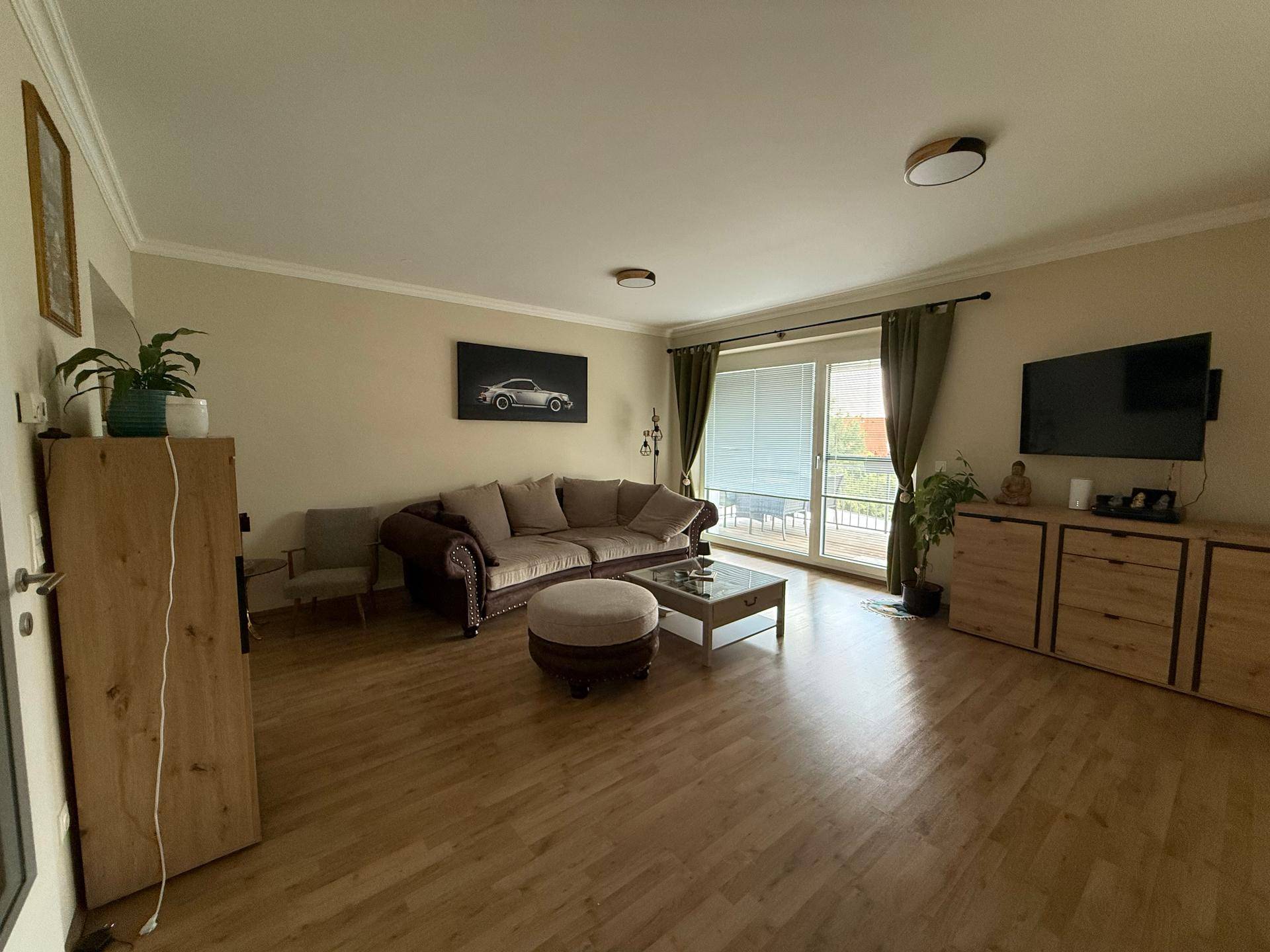 Geräumiges Wohnzimmer mit beigem Sofa, Laminatboden und Zugang zum Balkon.