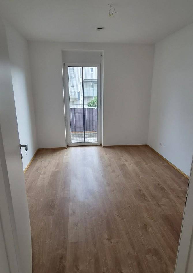 Helles Schlafzimmer mit Laminatboden und direktem Zugang zu einem Balkon.