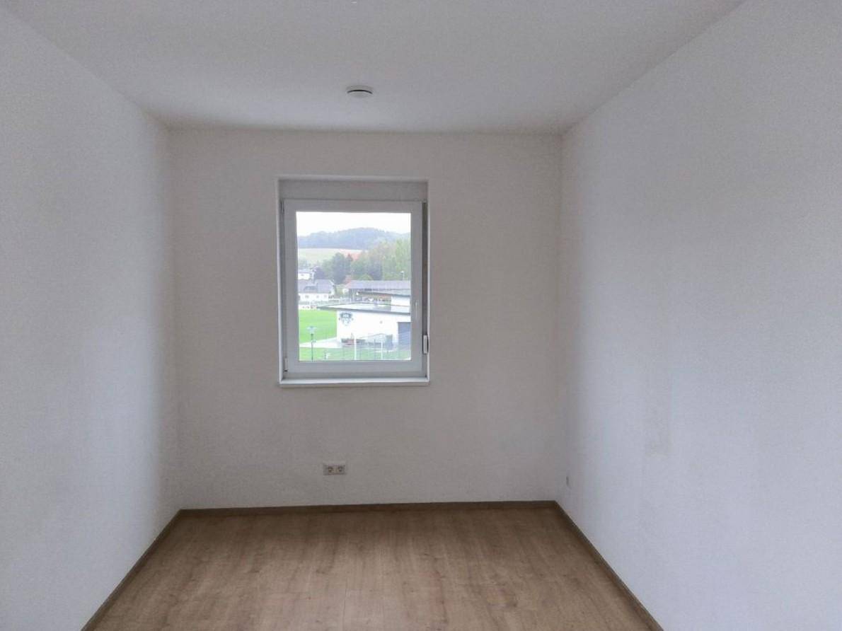 Ruhiges Schlafzimmer mit Laminatboden und Blick ins Grüne durch das Fenster.