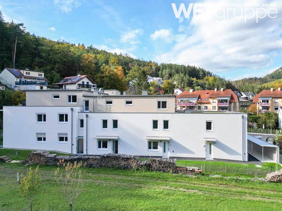 Panoramablick auf das moderne Wohngebäude in einer grünen, hügeligen Landschaft mit weiteren Häusern.