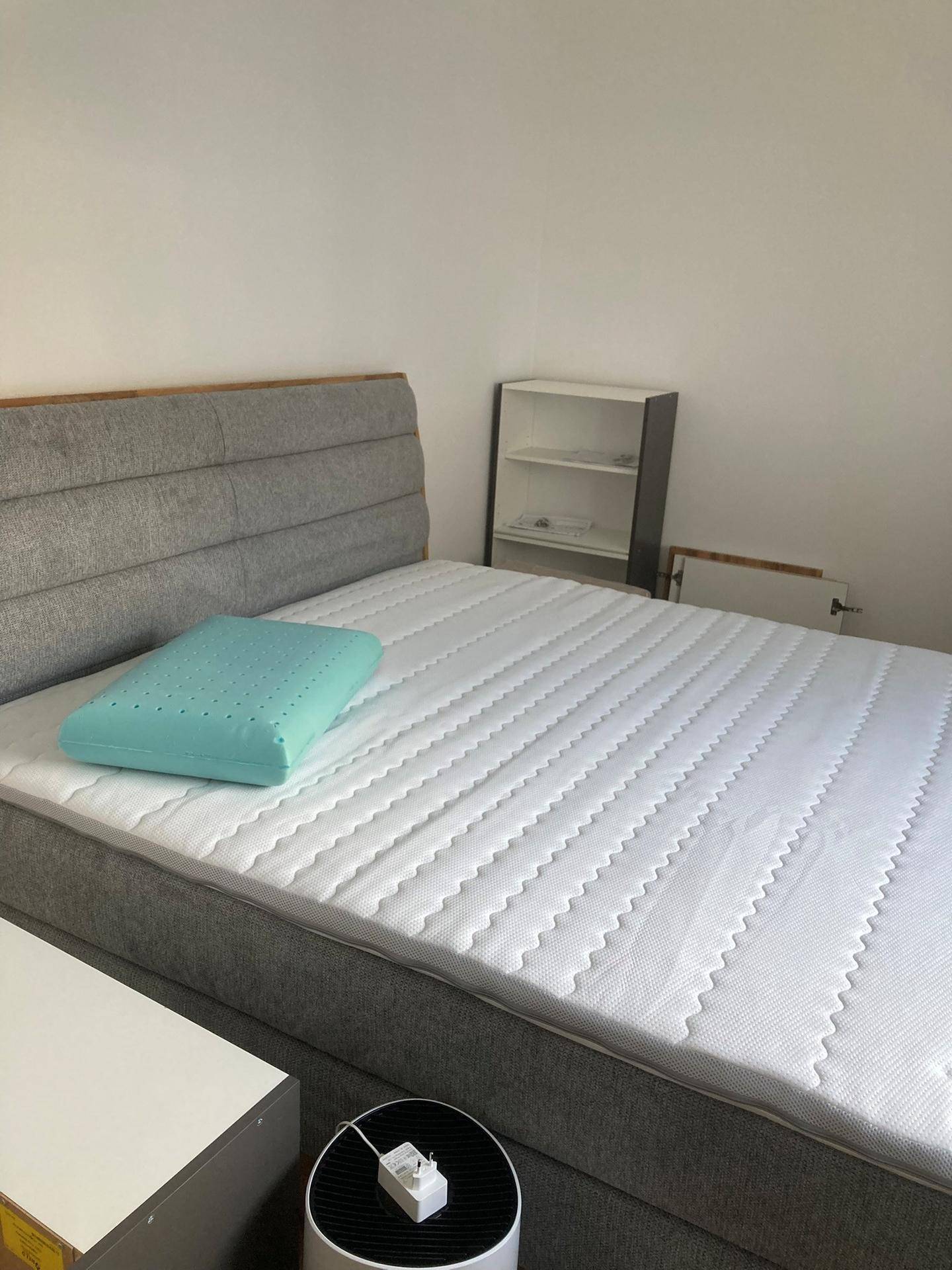 Helles Schlafzimmer mit modernem Bett, grauer Polsterung und minimalistischem Regal.