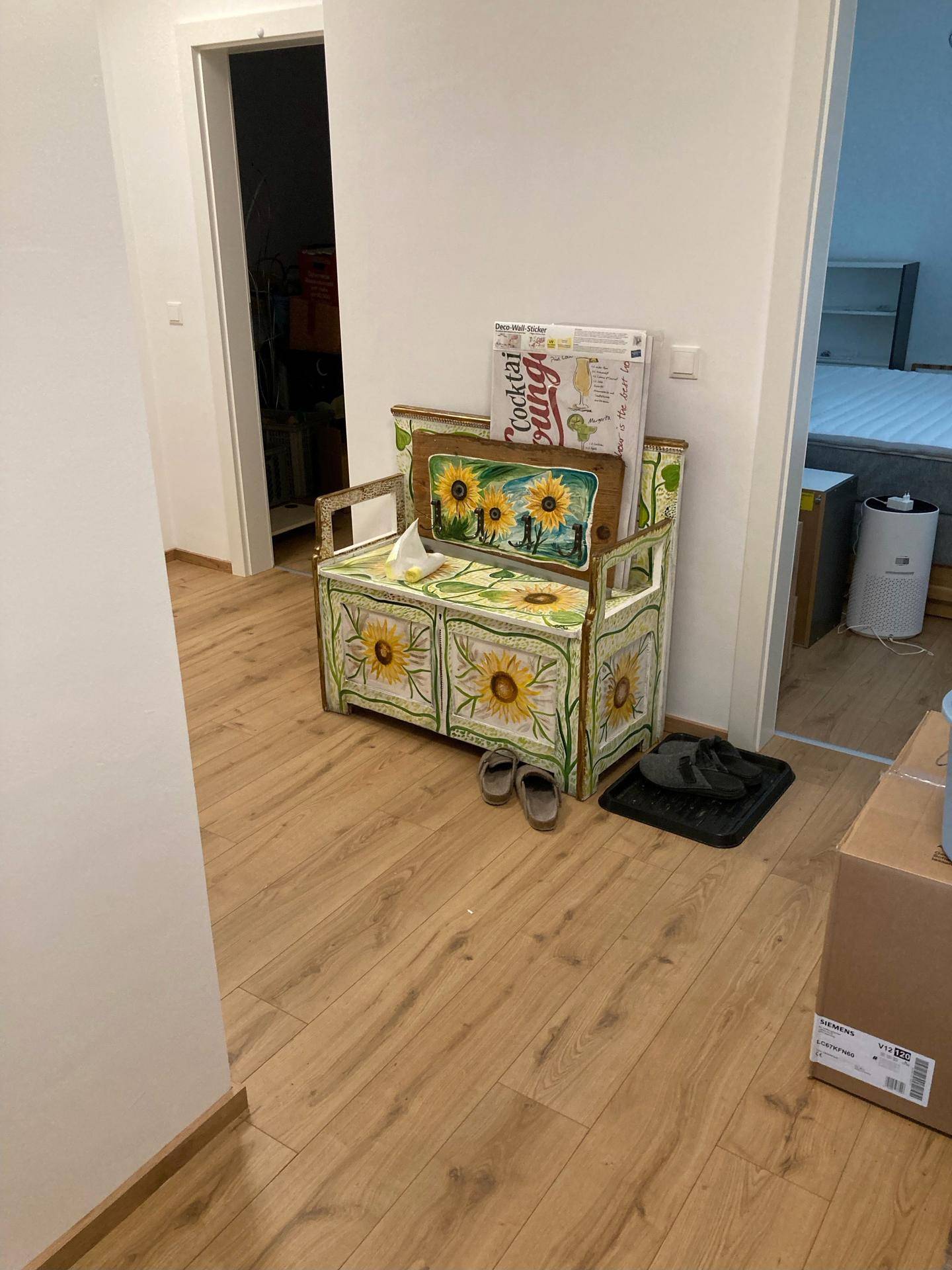 Flur mit Holzboden und einer farbenfrohen, sonnenblumenbemalten Sitzbank als Dekoration.