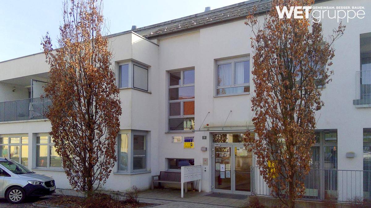 Ansicht eines modernen Wohngebäudes mit weißer Fassade, großen Fenstern und Bäumen im Vordergrund.