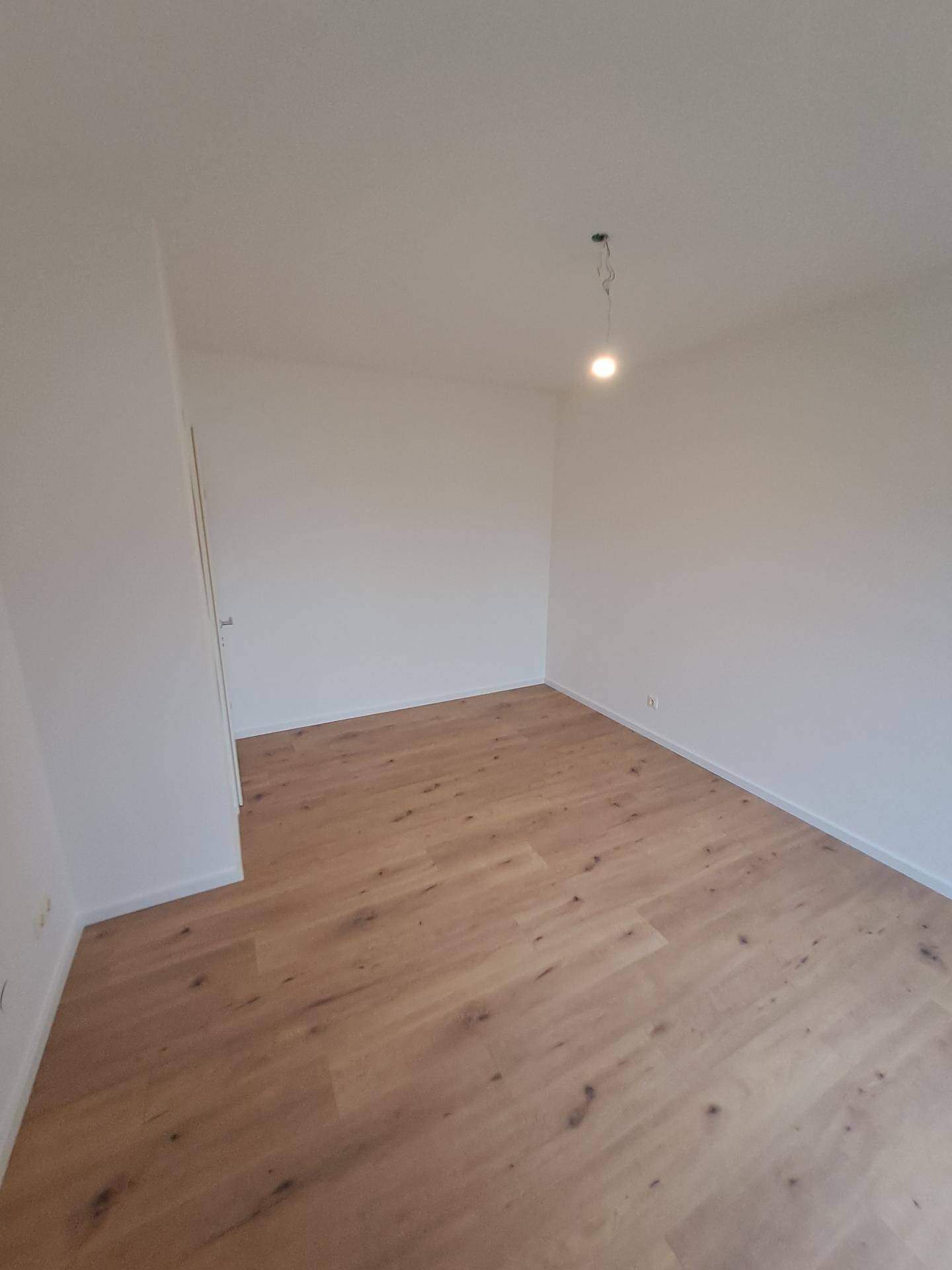 Leeres Zimmer mit hellem Holzboden und weißen Wänden, bereit zur individuellen Gestaltung.