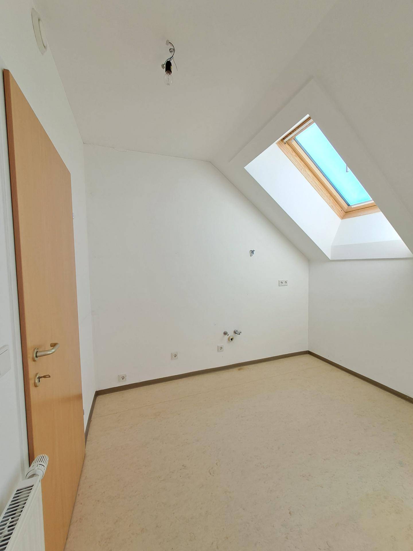 Leeres Zimmer mit Dachschräge, Laminatboden und einem Dachfenster für viel Tageslicht.
