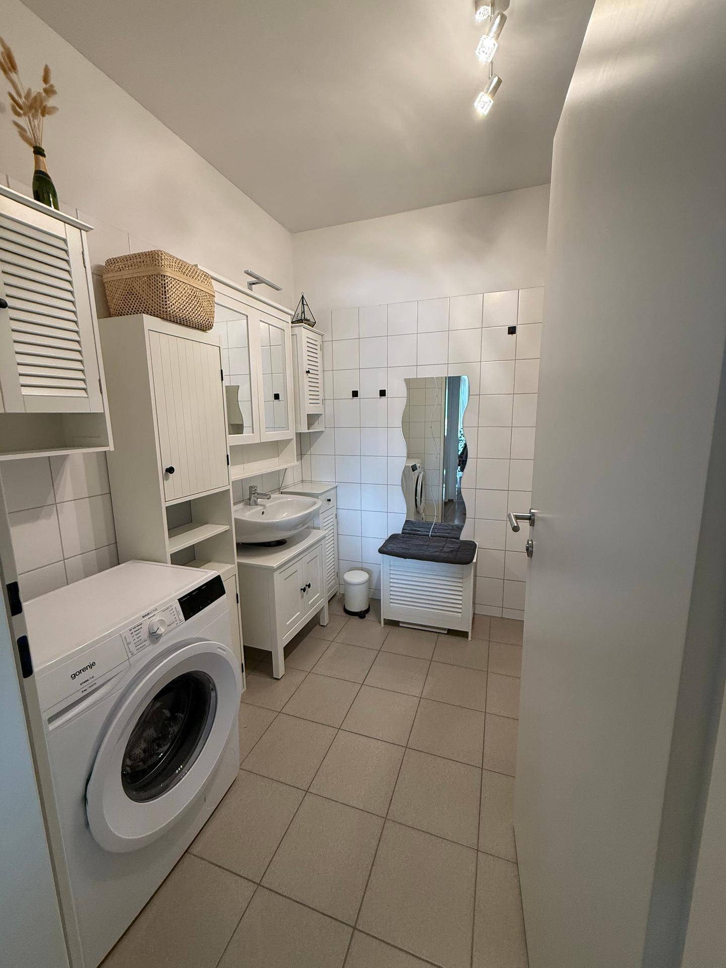 Helles Badezimmer mit Waschmaschine, Waschbecken und weißen Fliesen.