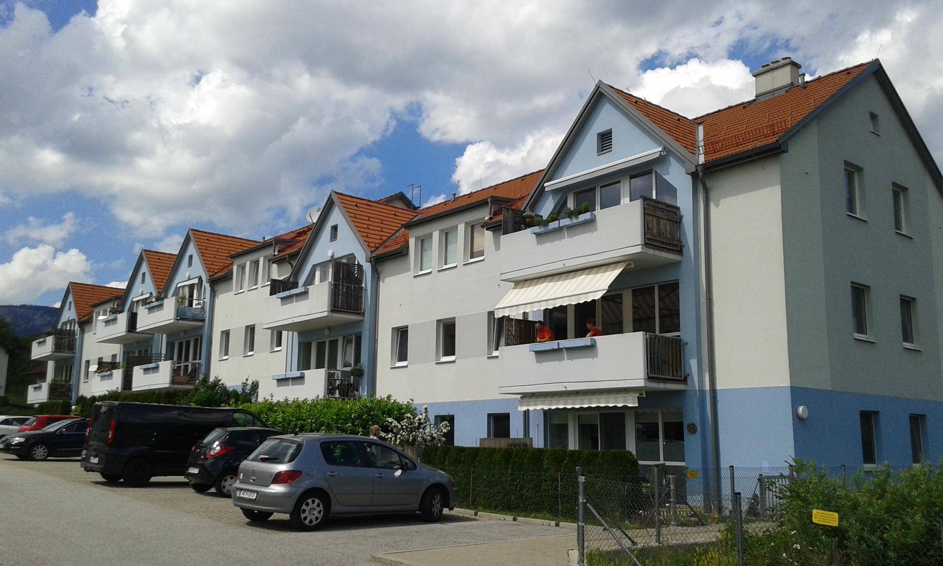 Wohngebäude mit Balkonen, blau-grauen Fassaden, rotem Ziegeldach und Blick auf die Berge.
