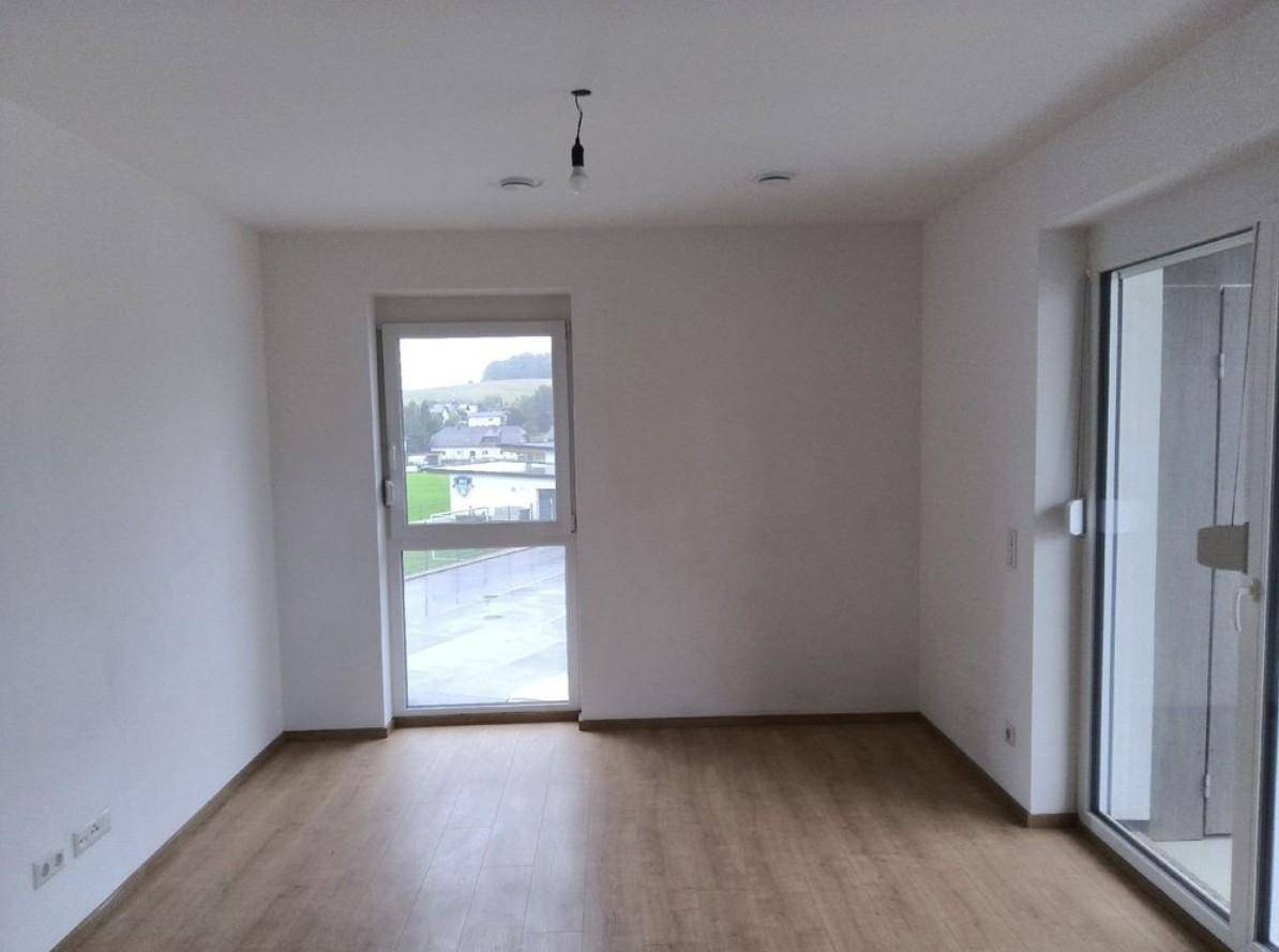 Helles Zimmer mit Laminatboden, großem Fenster und Zugang zu einem Balkon.