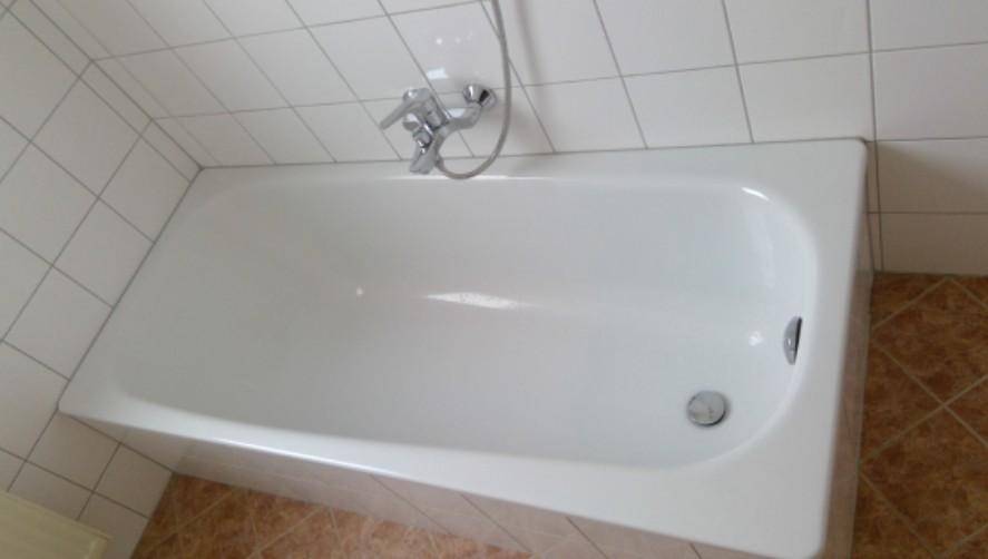 Einfaches Badezimmer mit weißer Badewanne und hellbraunen Fliesen an Boden und Wänden.