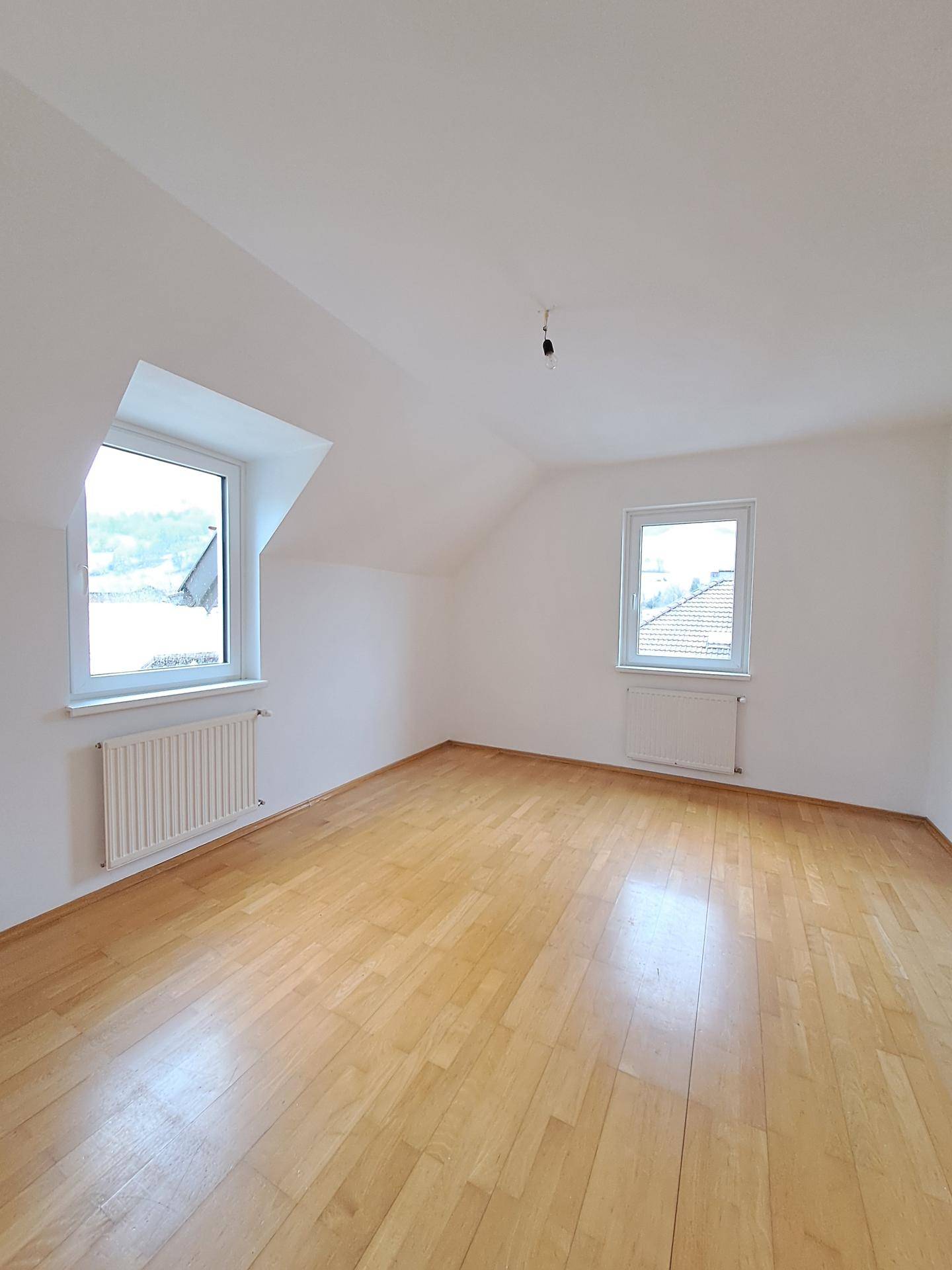 Geräumiger, heller Raum mit Laminatboden, Dachschrägen und zwei Fenstern, bereit zur individuellen Gestaltung.