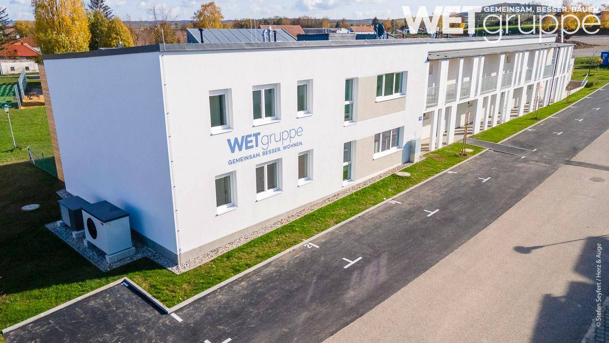Luftaufnahme der modernen Wohnanlage mit weißer Fassade und angrenzenden Parkflächen.