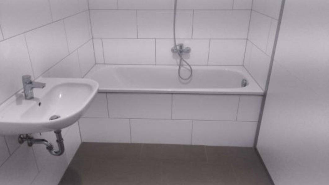 Einfaches Badezimmer mit Badewanne, Waschbecken und weißen Fliesen.