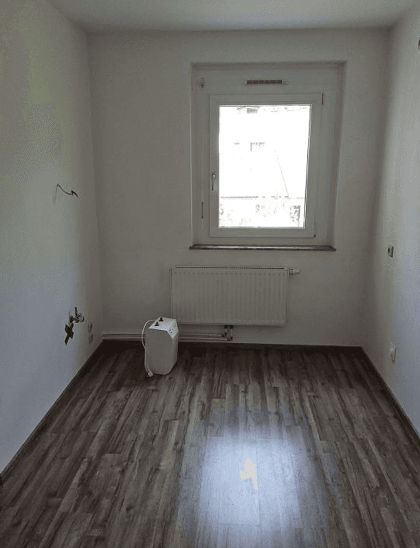 Leerer Raum mit Fenster, Heizkörper und Anschlüssen, ideal für eine kleine Küche oder Abstellraum.