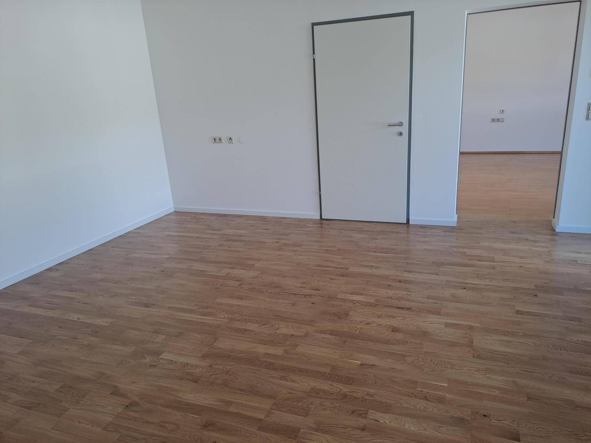Heller Innenraum mit Holzboden und weiß gestrichenen Wänden, der zu weiteren Räumen führt.