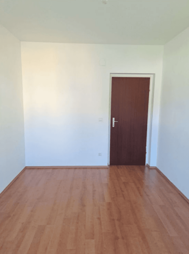 Leerer Raum mit Laminatboden und einer Holztür, bereit zur individuellen Gestaltung und Nutzung.