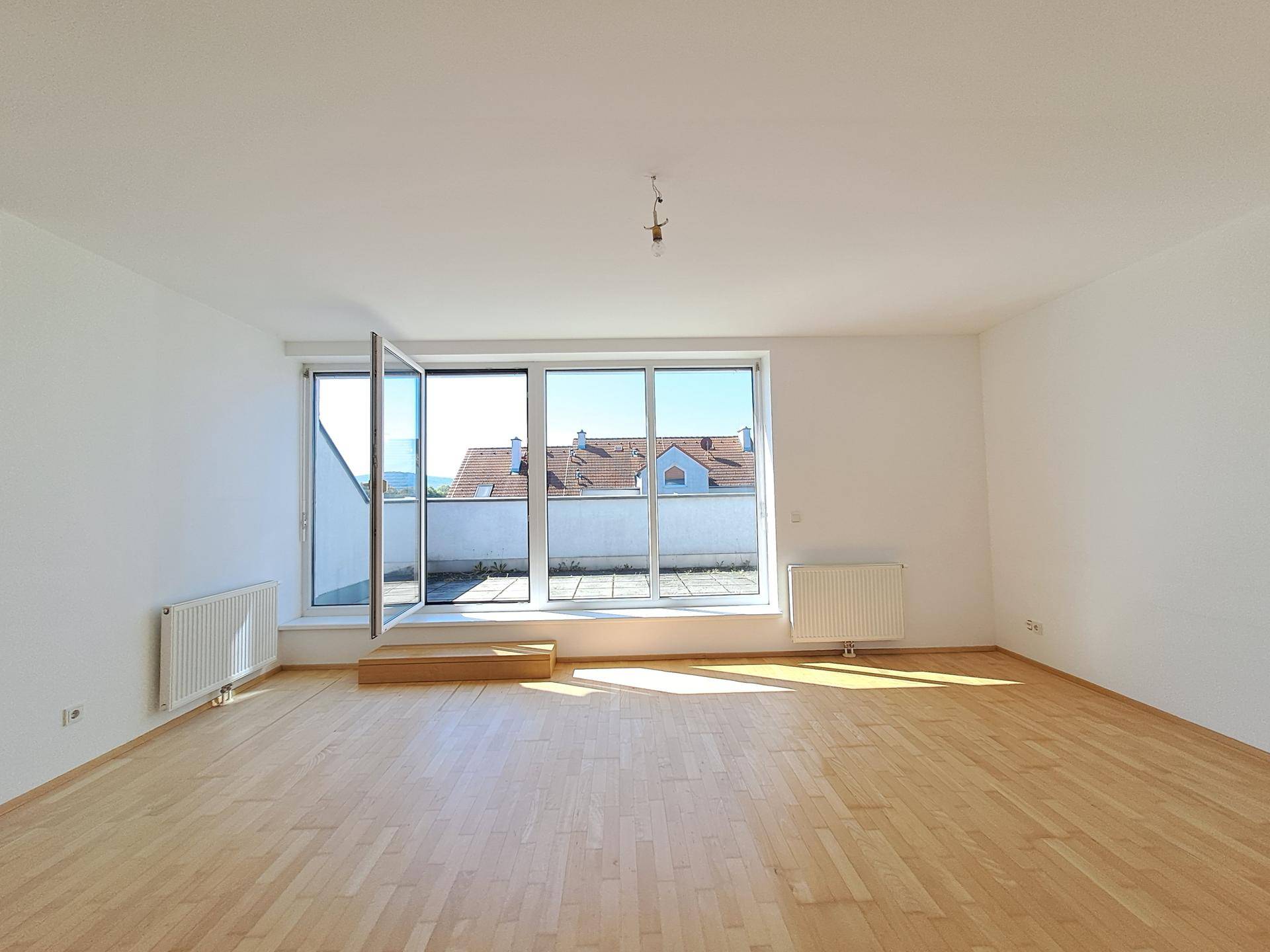 Großes Wohnzimmer mit hellem Parkettboden und Zugang zu einer sonnigen Terrasse.