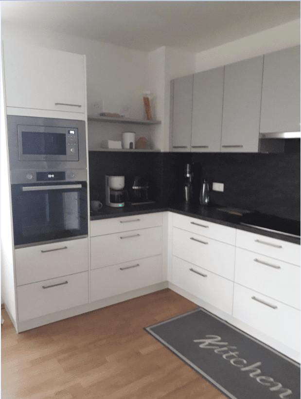 Moderne Küche mit weißen und grauen Schränken, integriertem Backofen und Mikrowelle.
