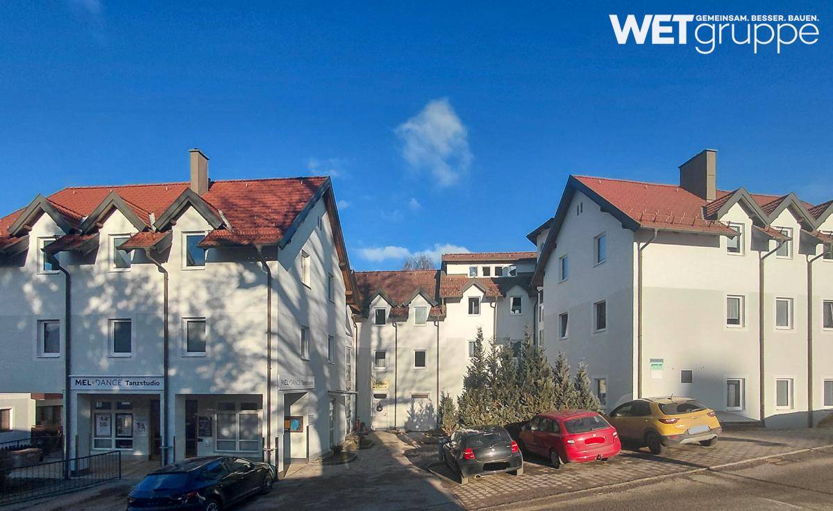 Mehrere Wohngebäude mit roten Dächern und Parkplätzen unter einem strahlend blauen Himmel in ländlicher Umgebung.