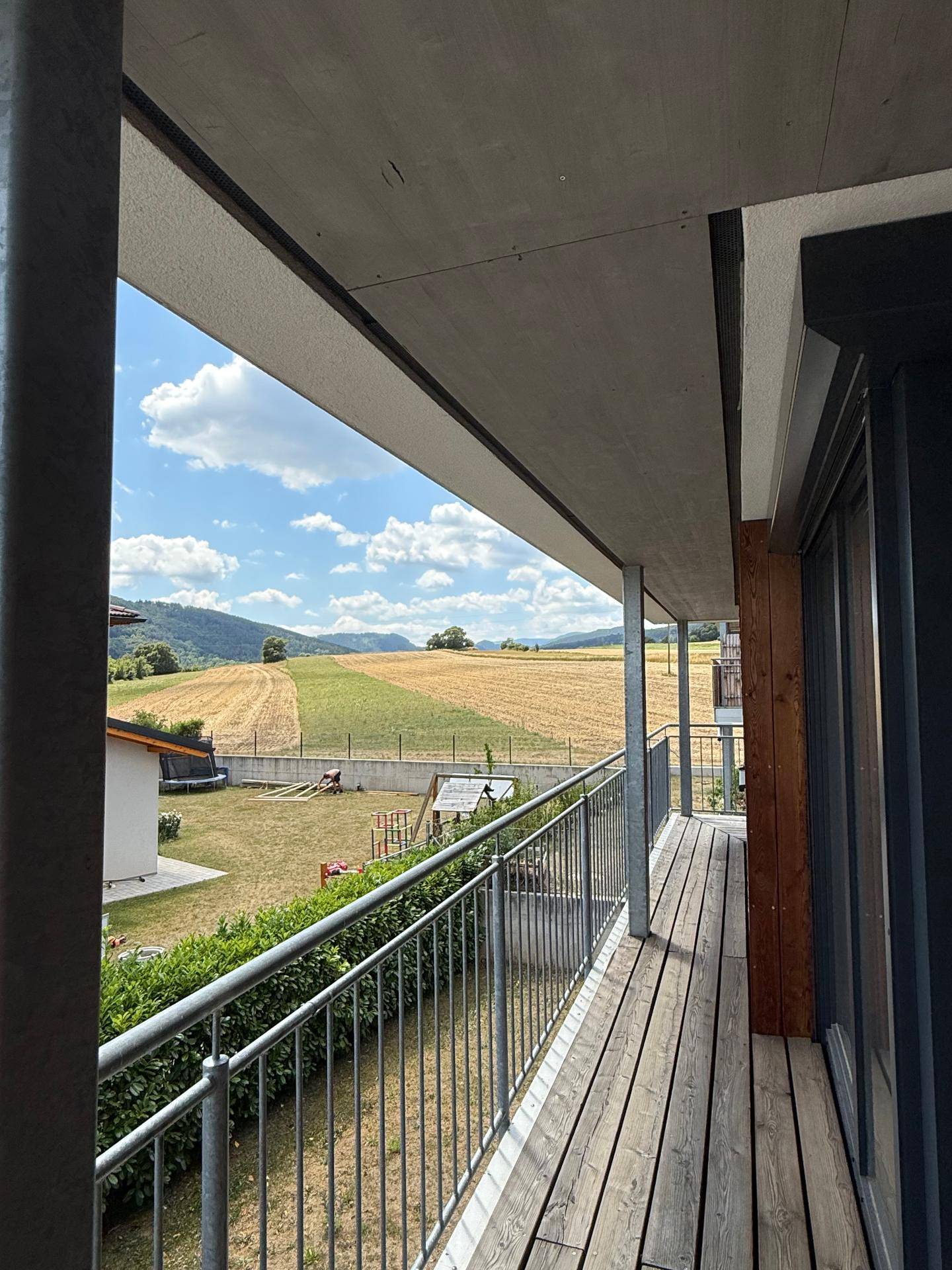 Langer Balkon mit Holzboden und weitem Blick über Felder und Hügel.