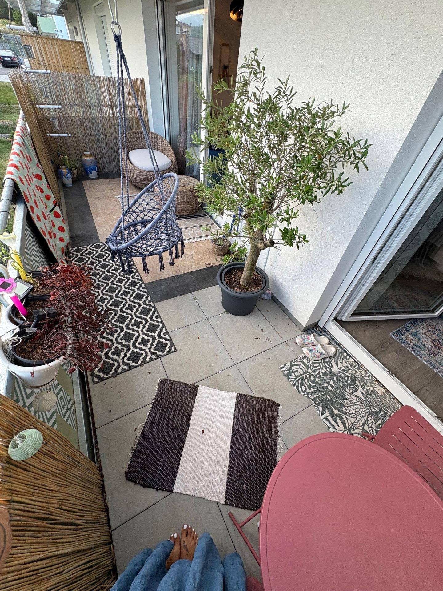 Kleiner Balkon mit Fliesenboden, Pflanzen und einem Hängesessel, ideal zum Entspannen.