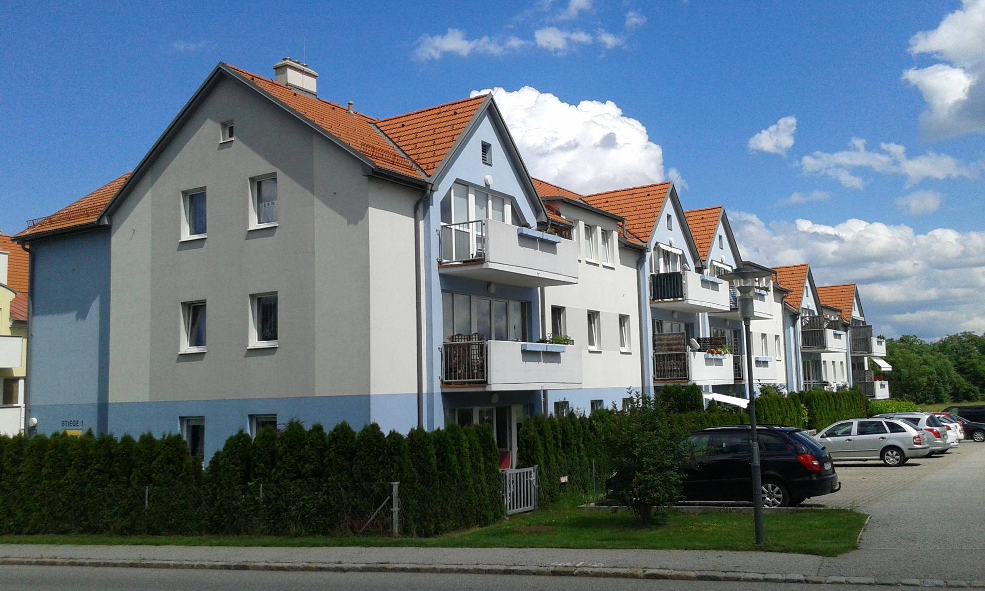 Reihen von Mehrfamilienhäusern mit Balkonen, blau-grauen Fassaden und rotem Ziegeldach.