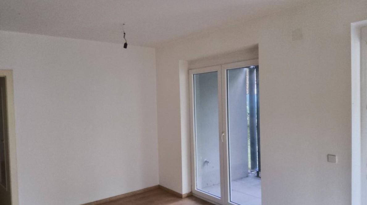Unmöblierter Raum mit hellem Fenster und Zugang zu einem Balkon oder einer kleinen Terrasse.