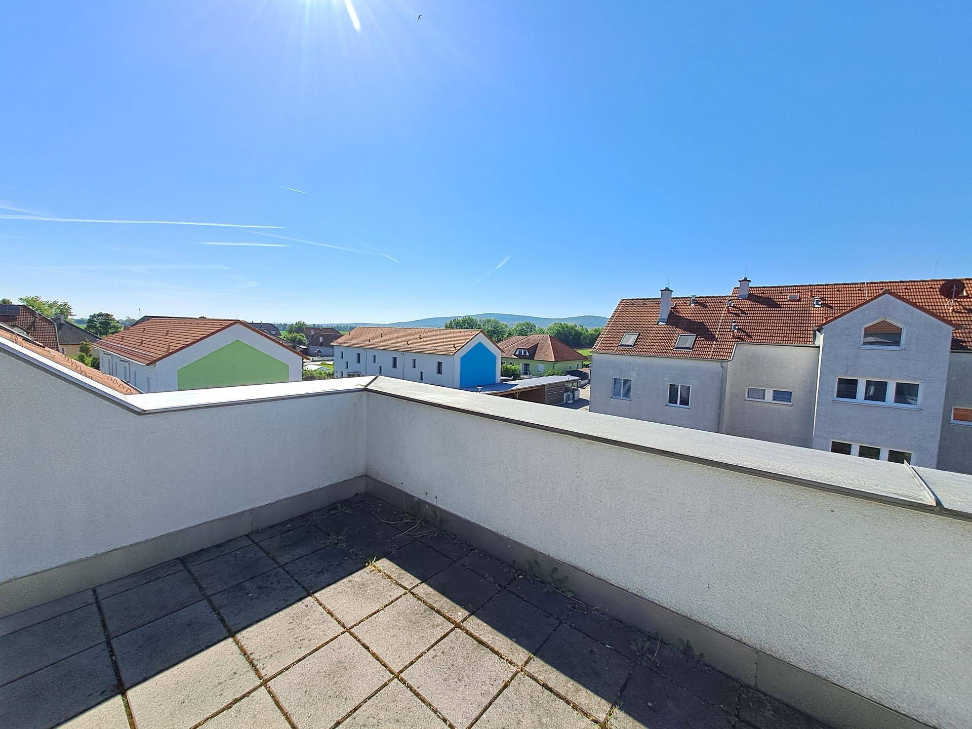 Geräumige Terrasse mit Fliesenboden und weitem Blick über die Dächer und Landschaft.