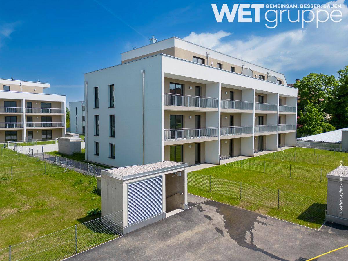 Modernes Wohngebäude mit Balkonen und einer Tiefgaragenzufahrt, umgeben von Rasenflächen.