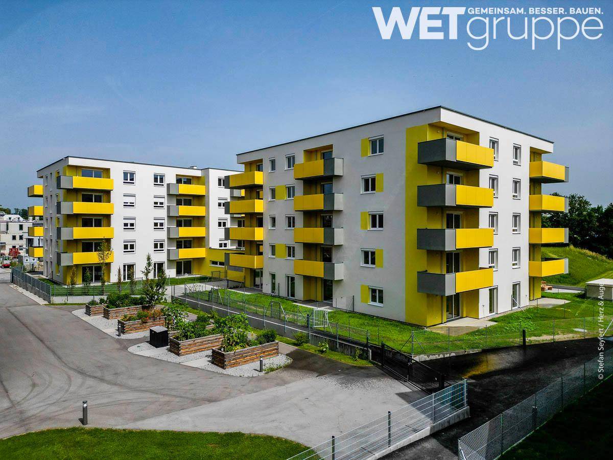 Moderne Wohngebäude mit leuchtend gelben Balkonen und gemeinschaftlichen Hochbeeten.
