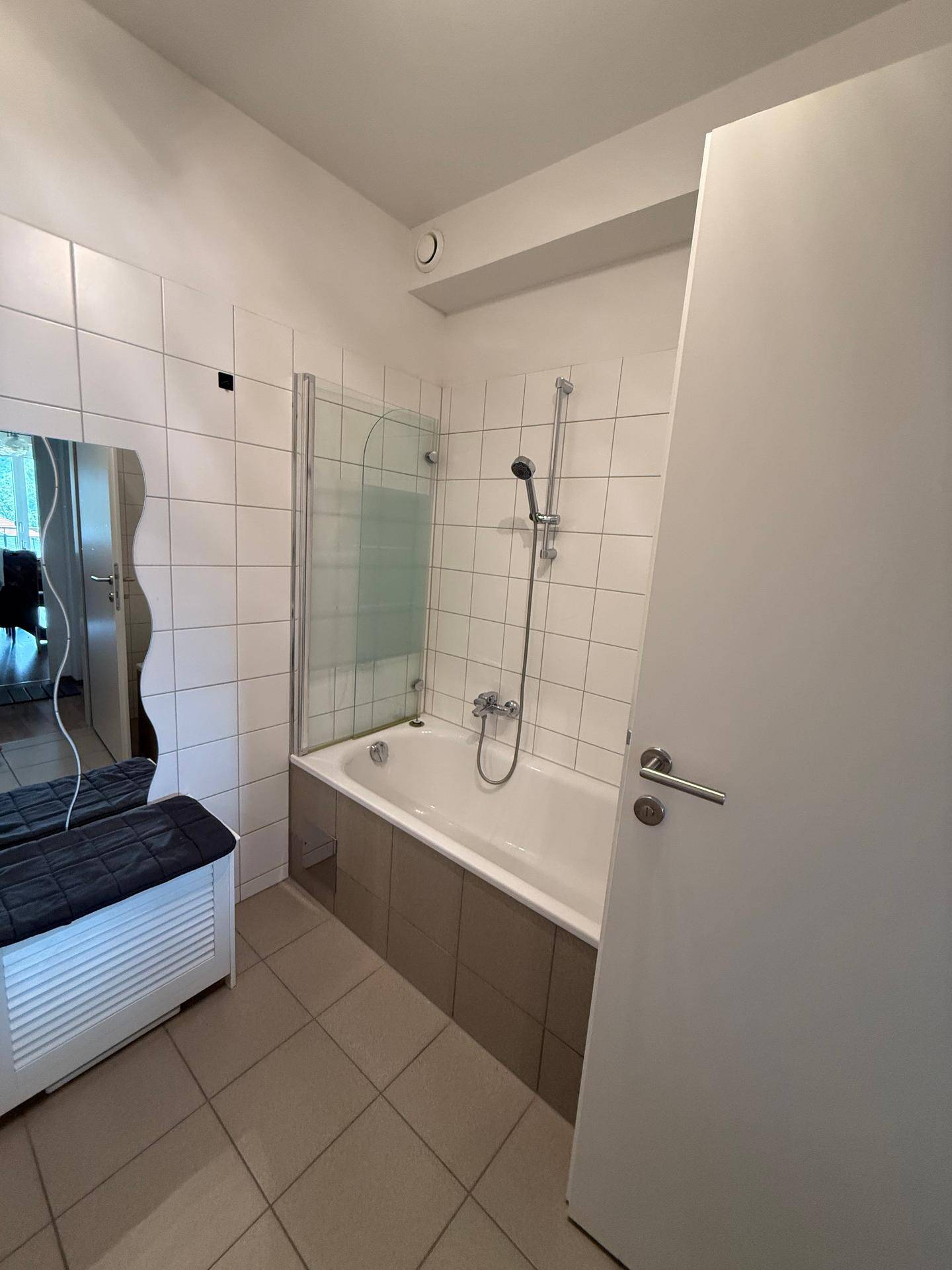Badezimmer mit Badewanne, Duschabtrennung und hellen Fliesen an Wänden und Boden.