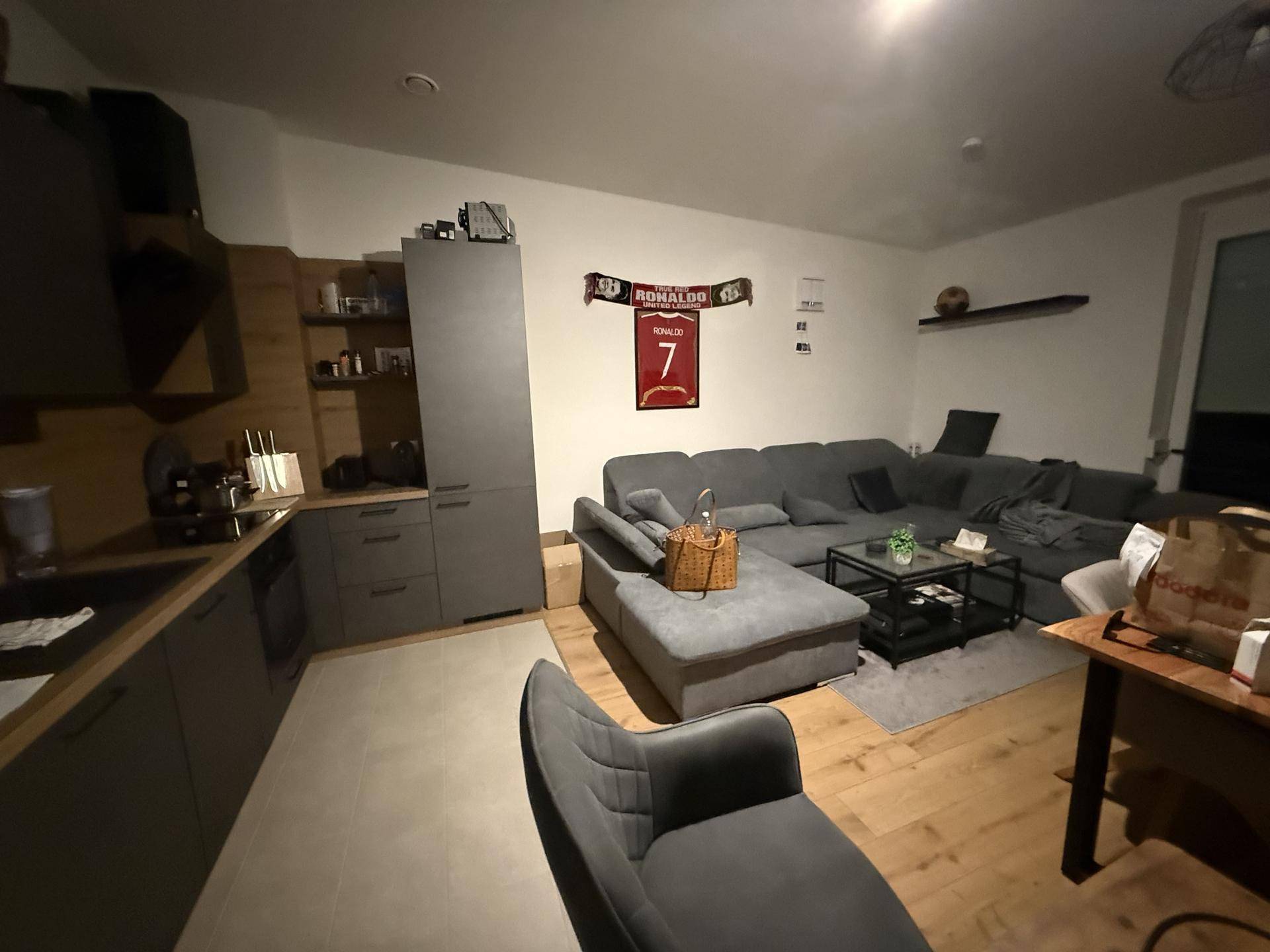 Moderner Wohnbereich mit grauer Eckcouch, Couchtisch und offener Küchenzeile.